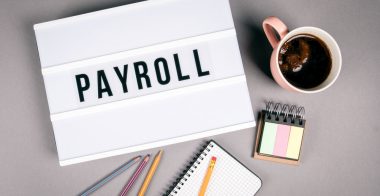 Payroll. Text in light box. Pink coffee mug on gray background Payroll. Text in light box. Pink coffee mug on gray background